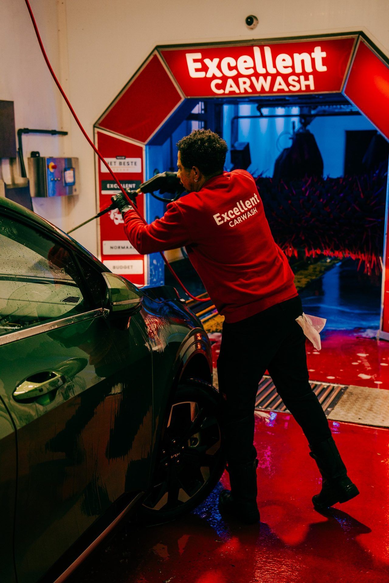 Handmatige voorwas van de zijkant van een auto, met de verlichte wasstraat op de achtergrond.