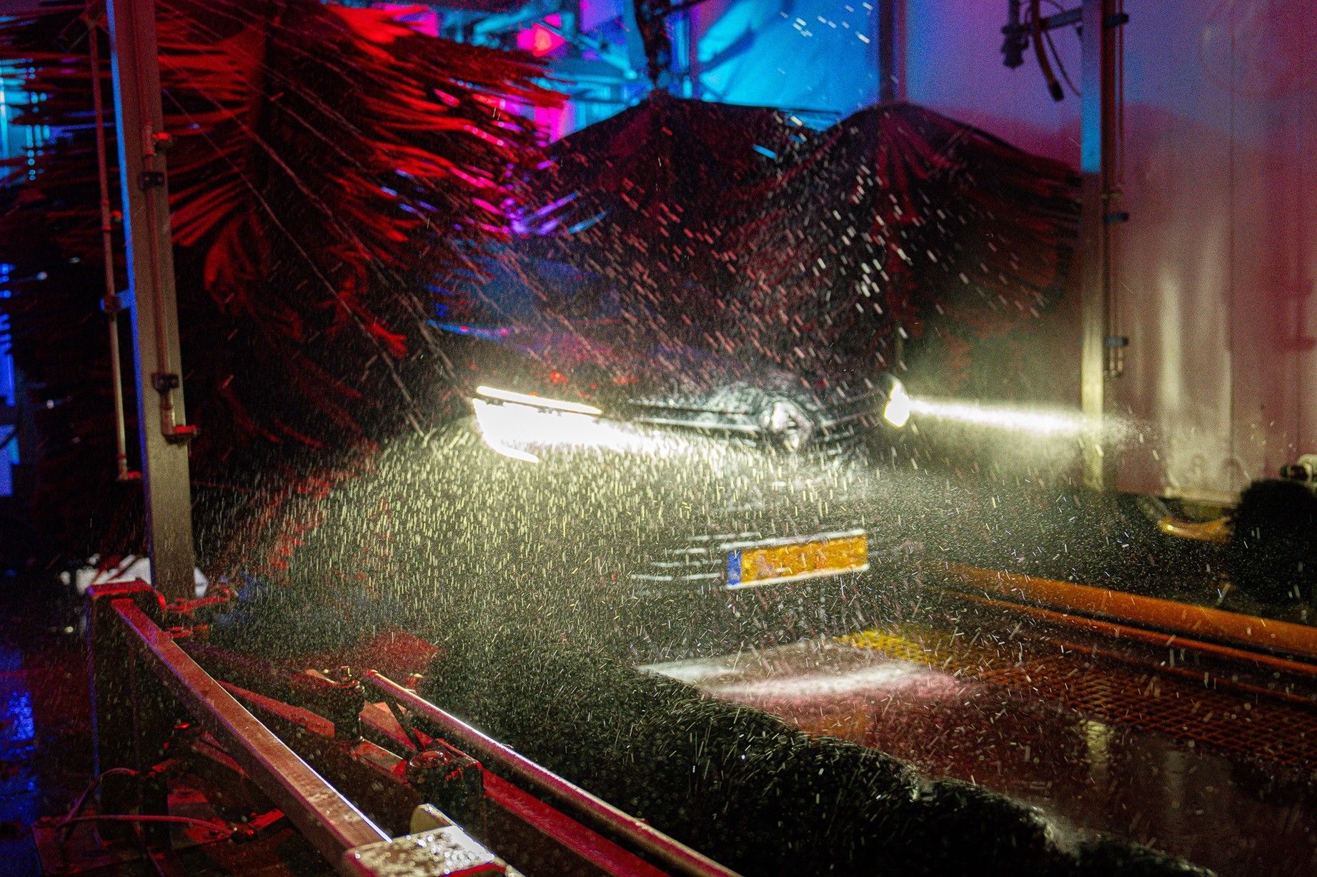 Auto in de wasstraat van Excellent Carwash tussen de rode textielborstels, met water en schuim.